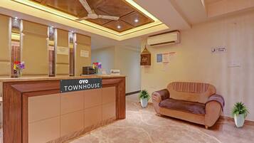 A reception desk labeled 'OYO TOWNHOUSE' with a ceiling fan, air conditioning unit, and a reception area with a couch and potted plants.