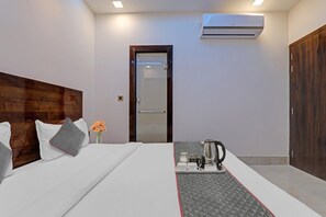 Quarto de hotel com cama, mesa de cabeceira com chaleira, um vaso com flores e ar condicionado.