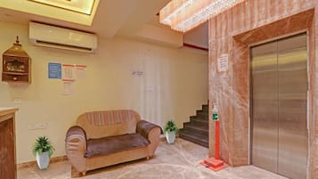 A lobby with a sofa, a staircase, an elevator, and a wall-mounted air conditioner.