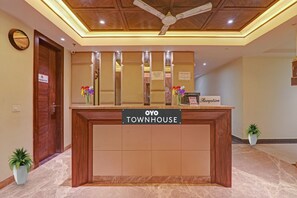 Bancada de recepção com a placa 'OYO TOWNHOUSE', um ventilador de teto, um relógio e uma placa indicando área de recepção.