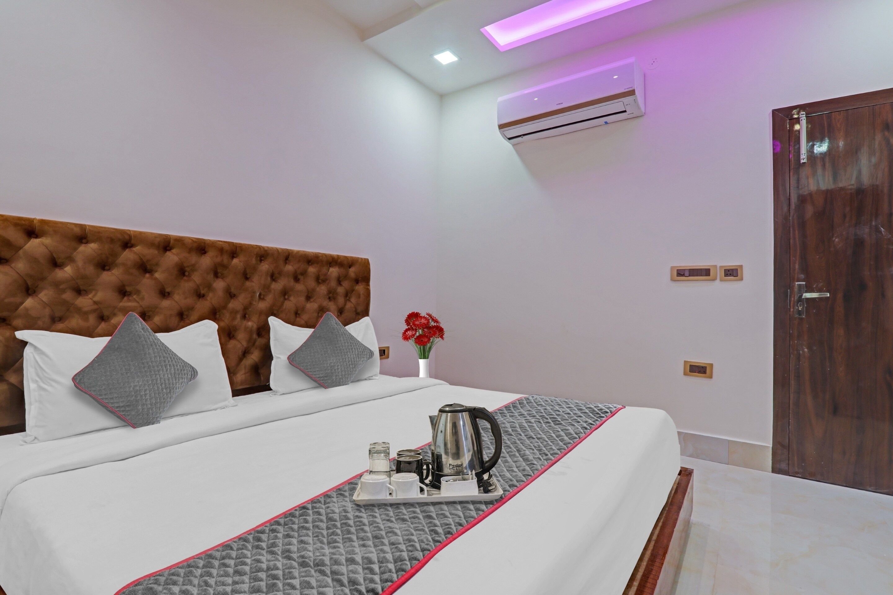 A hotel room with a large bed, a bedside table with a kettle, and a wall-mounted air conditioner.