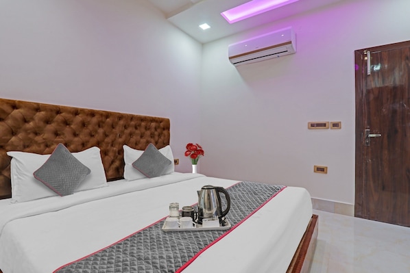 A hotel room with a large bed, a bedside table with a kettle, and a wall-mounted air conditioner.
