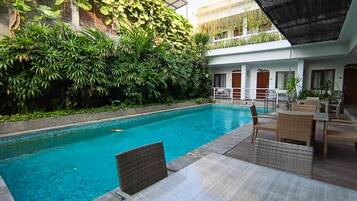 Una piscina con solárium de baldosas, rodeada de exuberante vegetación y mobiliario de exterior.