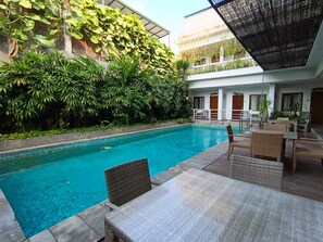 A swimming pool with a tiled deck, surrounded by lush greenery and outdoor furniture. - Townhouse Oak D'Lima Hotel Sunset Road (Legian)