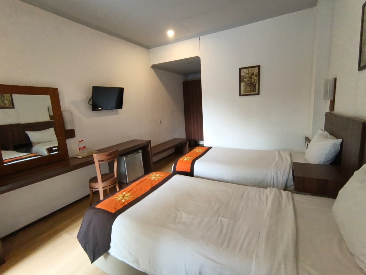 Habitación de hotel con dos camas, un escritorio, una silla, un televisor y un cuadro en la pared.