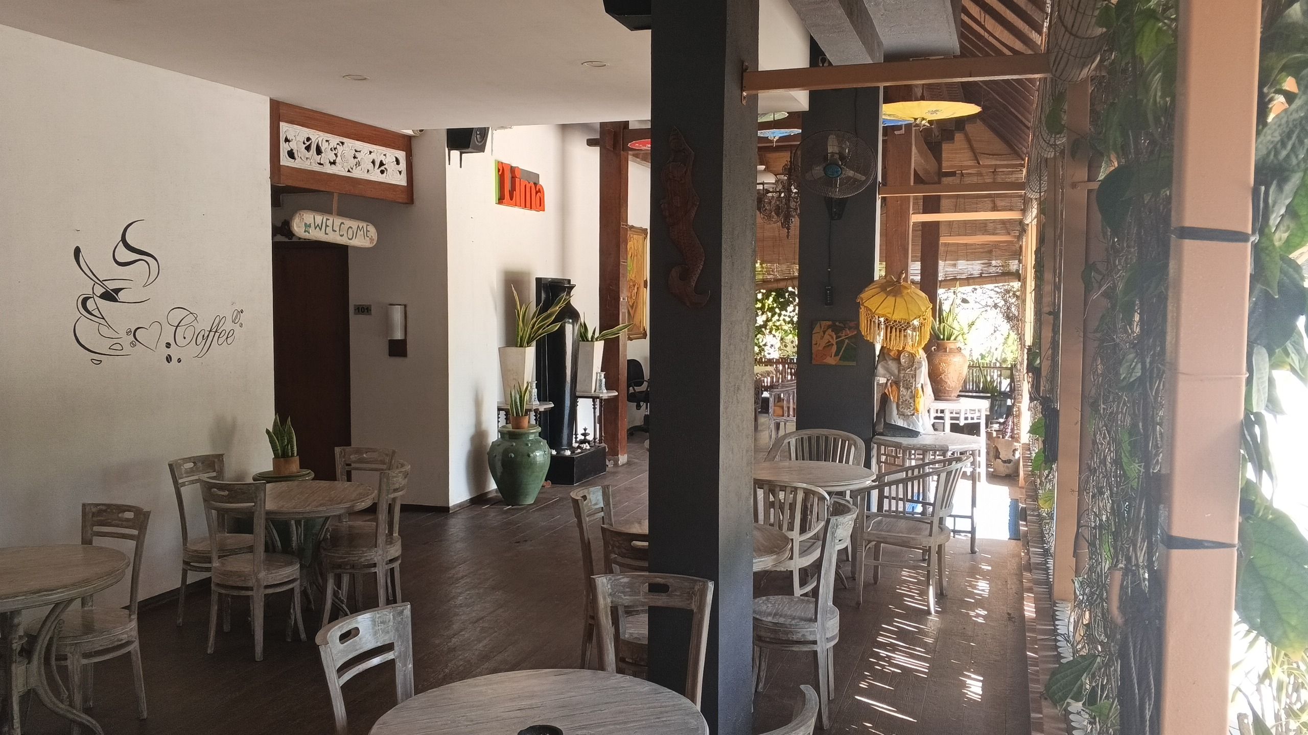 Un restaurant amb diverses taules i caires, un cartell que diu 'Welcome' i un rètol de 'Coffee' a la paret.