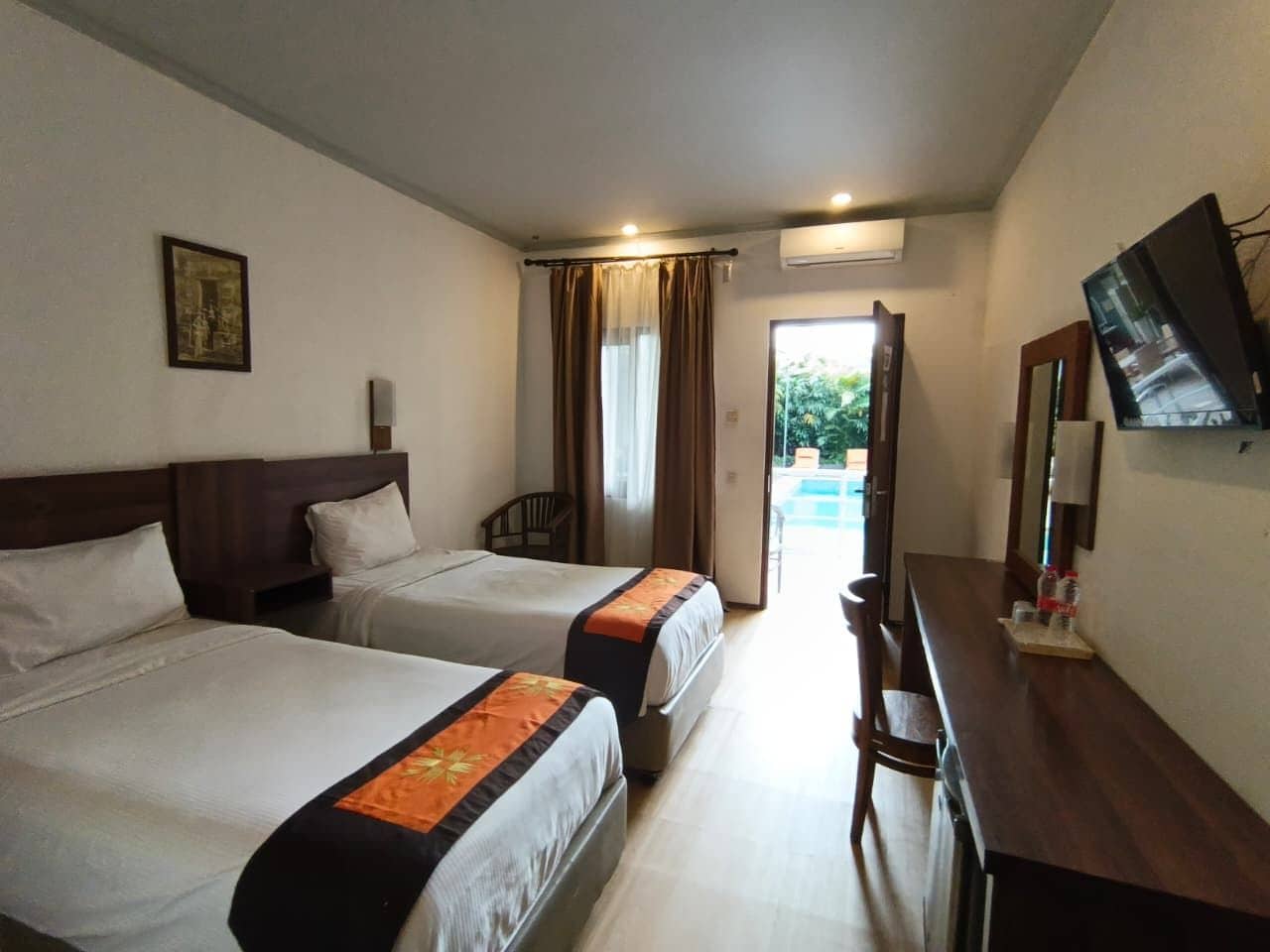 A hotel room with two beds, a desk, a chair, a television, and a window with curtains.