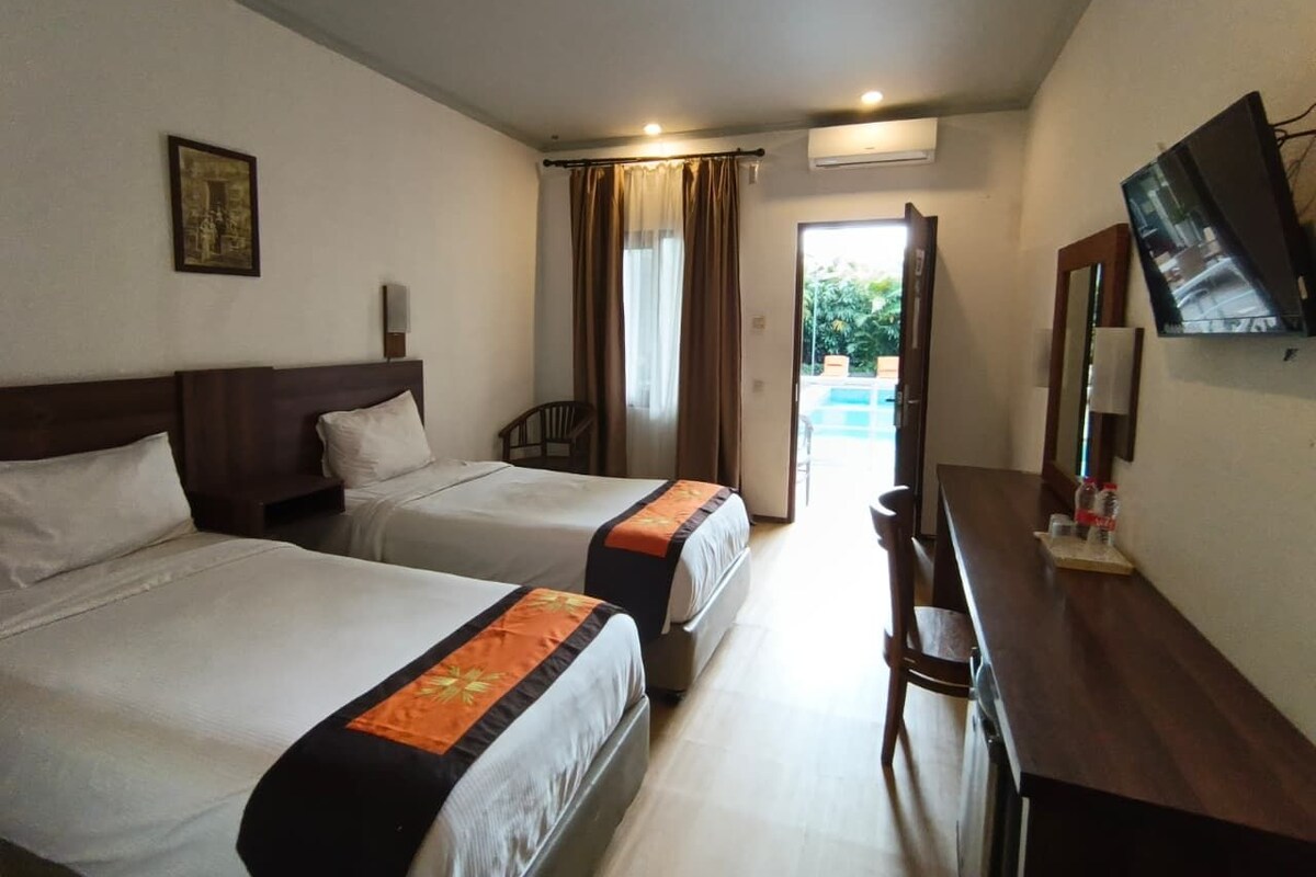 A hotel room with two beds, a desk, a chair, a television, and a window with curtains.