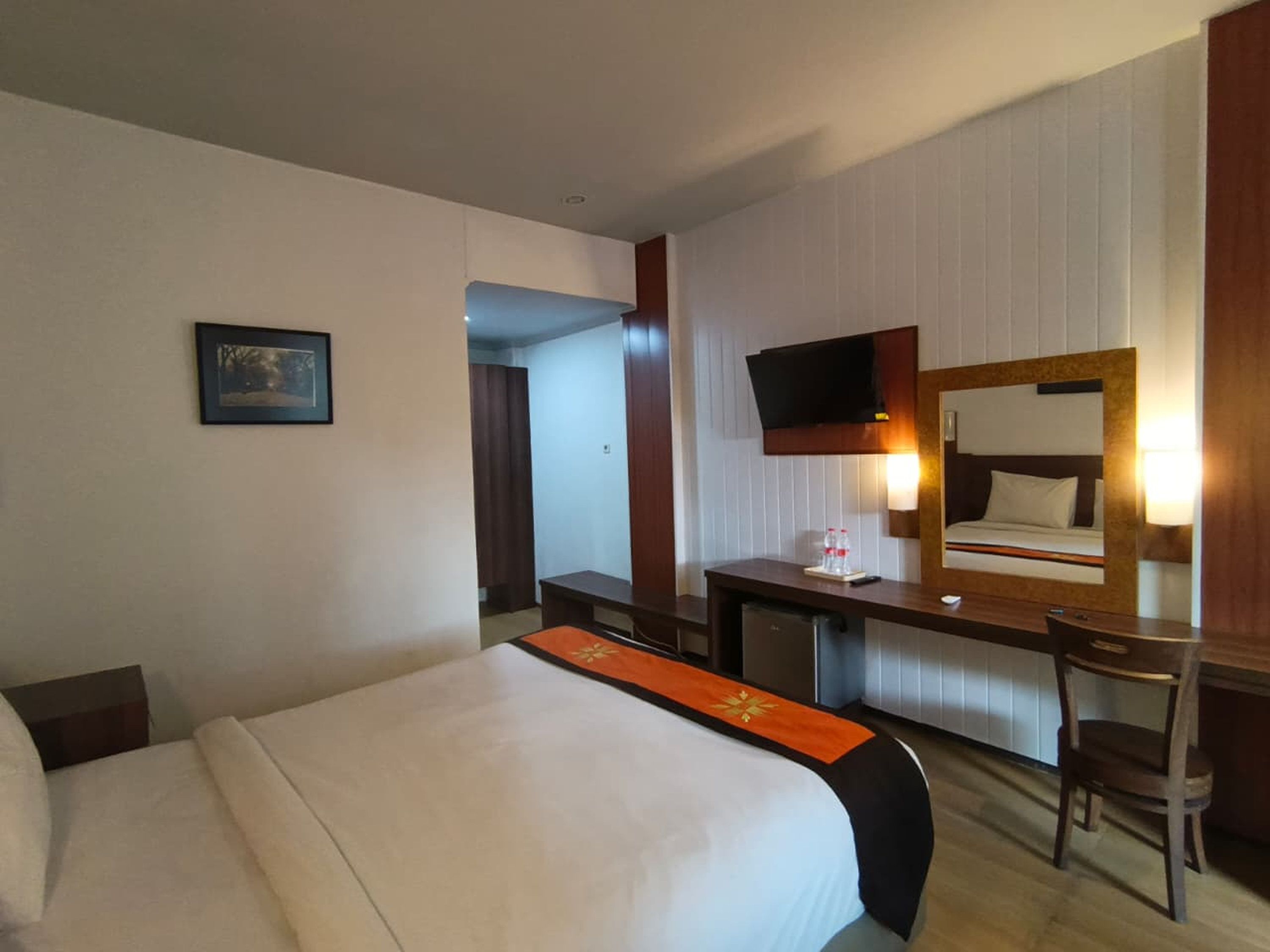 Habitació d'hotel amb llit, escriptori, cadira, televisió i mirall.