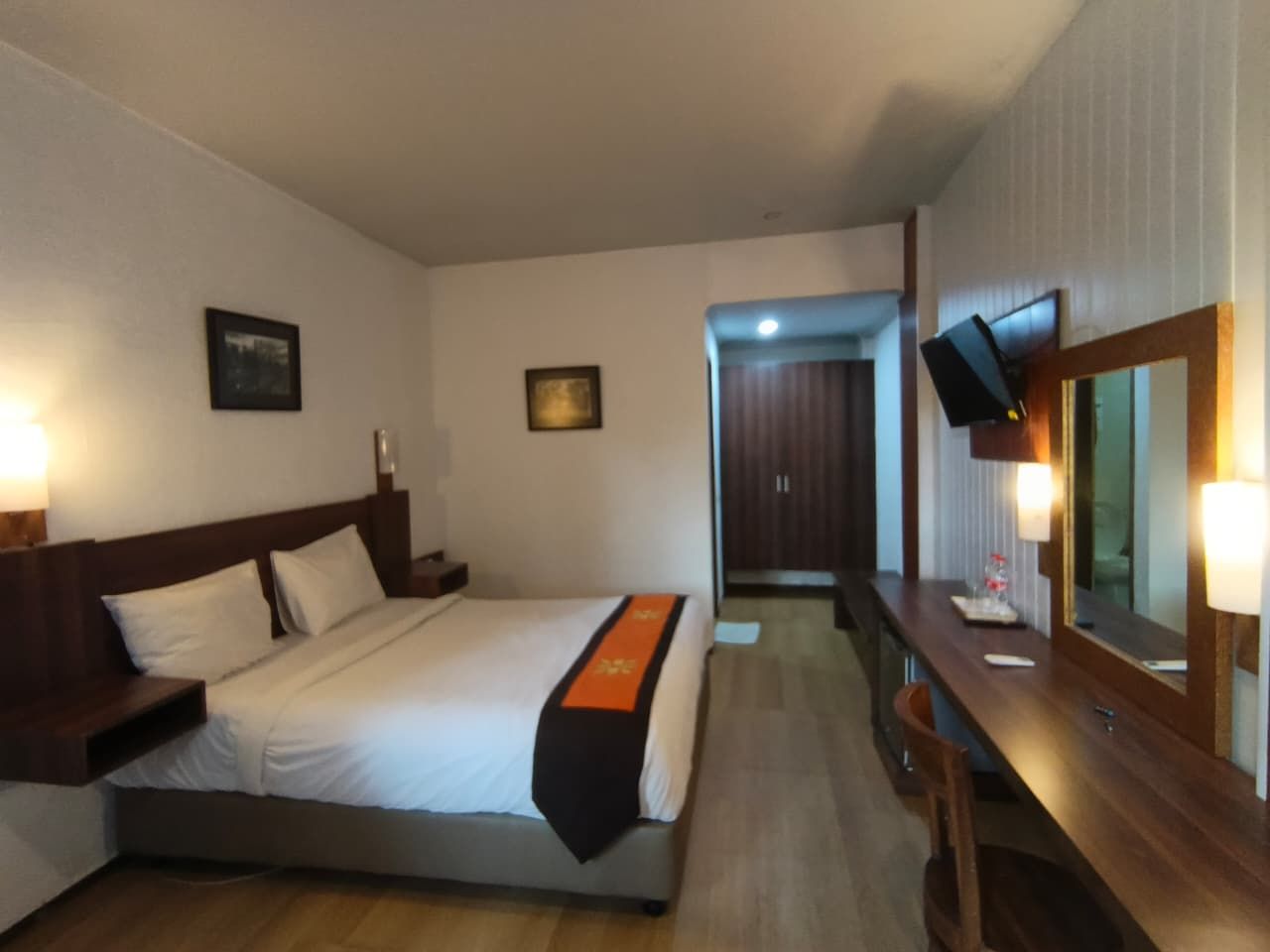 Una habitación de hotel con cama, mesita de noche, lámpara y espejo.