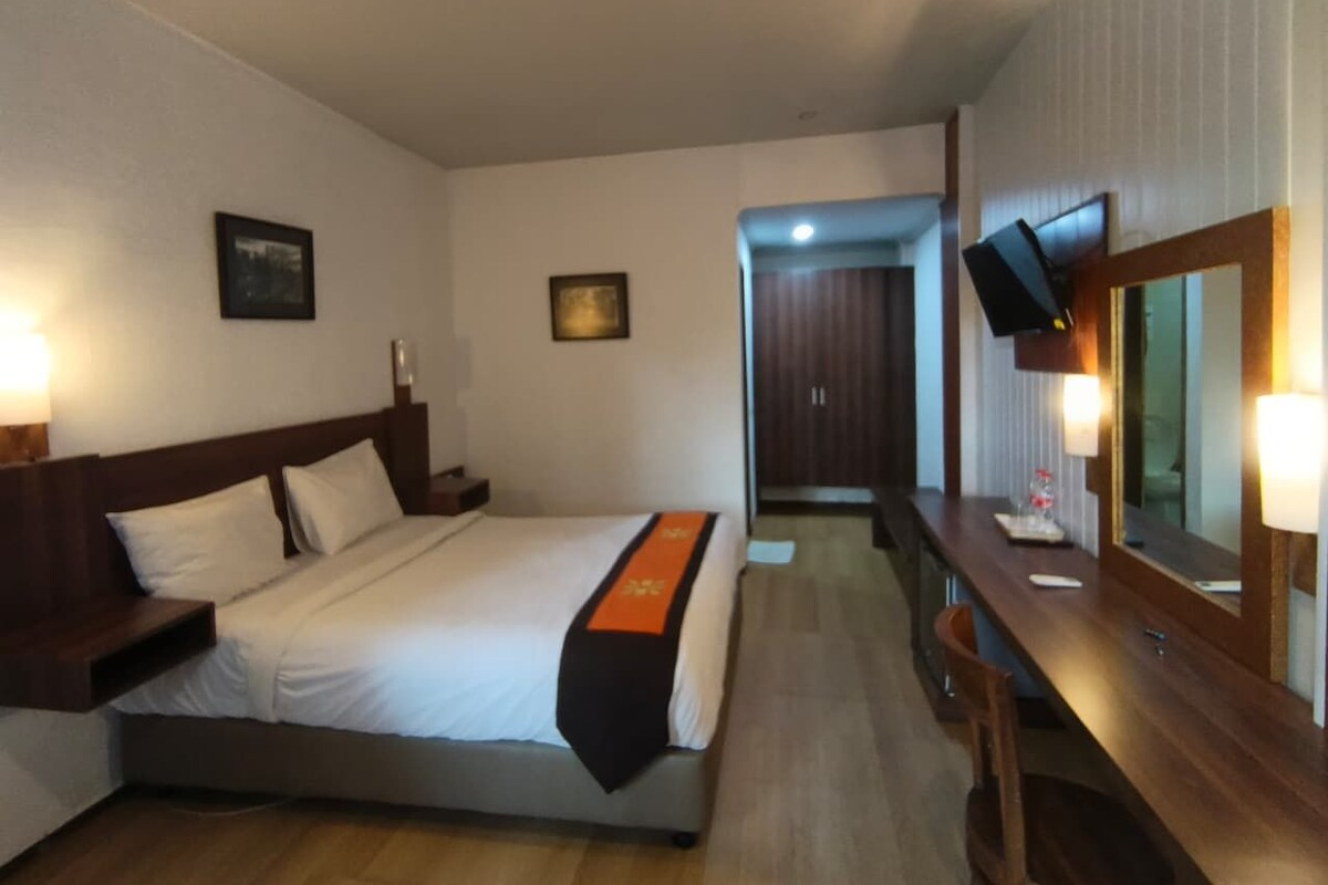 A hotel room with a bed, bedside table, lamp, and a mirror.