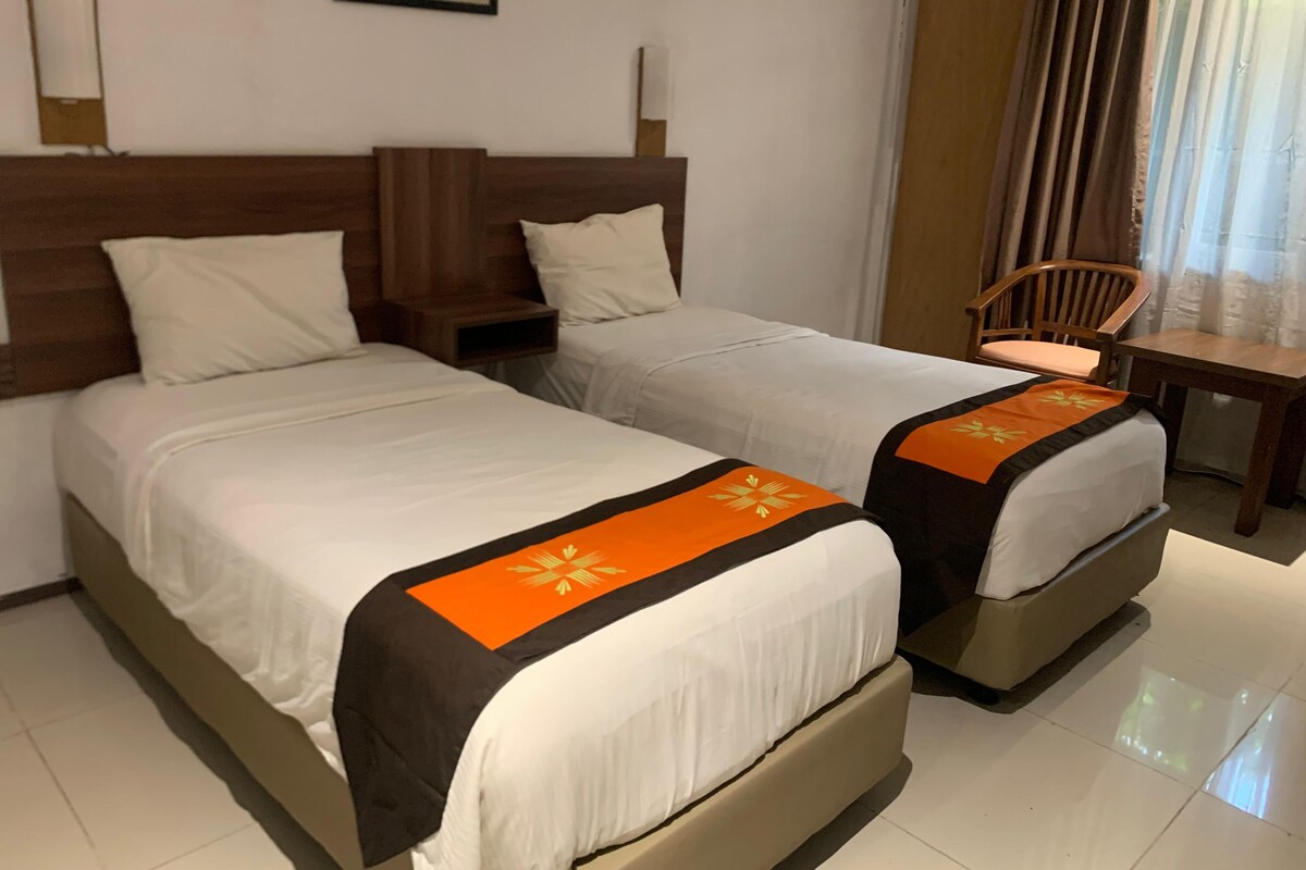 A hotel room with two beds, a wooden headboard, a small table, and a chair.