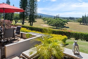 An outdoor seating area with a red umbrella, chairs, and a view of a golf course. - New Double-Rental: Stunning Ocean-View 4BR Kapalua Golf Villa | Luxury Group Getaway (Lahaina)