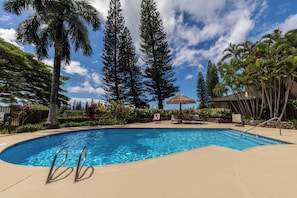 A swimming pool with a clear blue water, surrounded by palm trees and a stone wall. - New Double-Rental: Stunning Ocean-View 4BR Kapalua Golf Villa | Luxury Group Getaway (Lahaina)