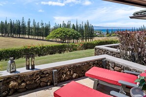 Un patio con muros de piedra, una zona de estar con cojines rojos y vistas a un jardín ajardinado y al océano.