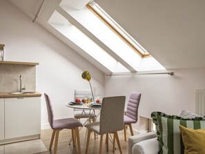 A modern dining area with a skylight, a kitchen with a sink, and a sofa with cushions. - Barbican Apartments by Fragola (Kraków)