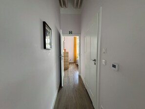 A hallway with a door leading to a bedroom, a framed picture on the wall, and a thermostat on the wall. - Barbican Apartments by Fragola (Kraków)