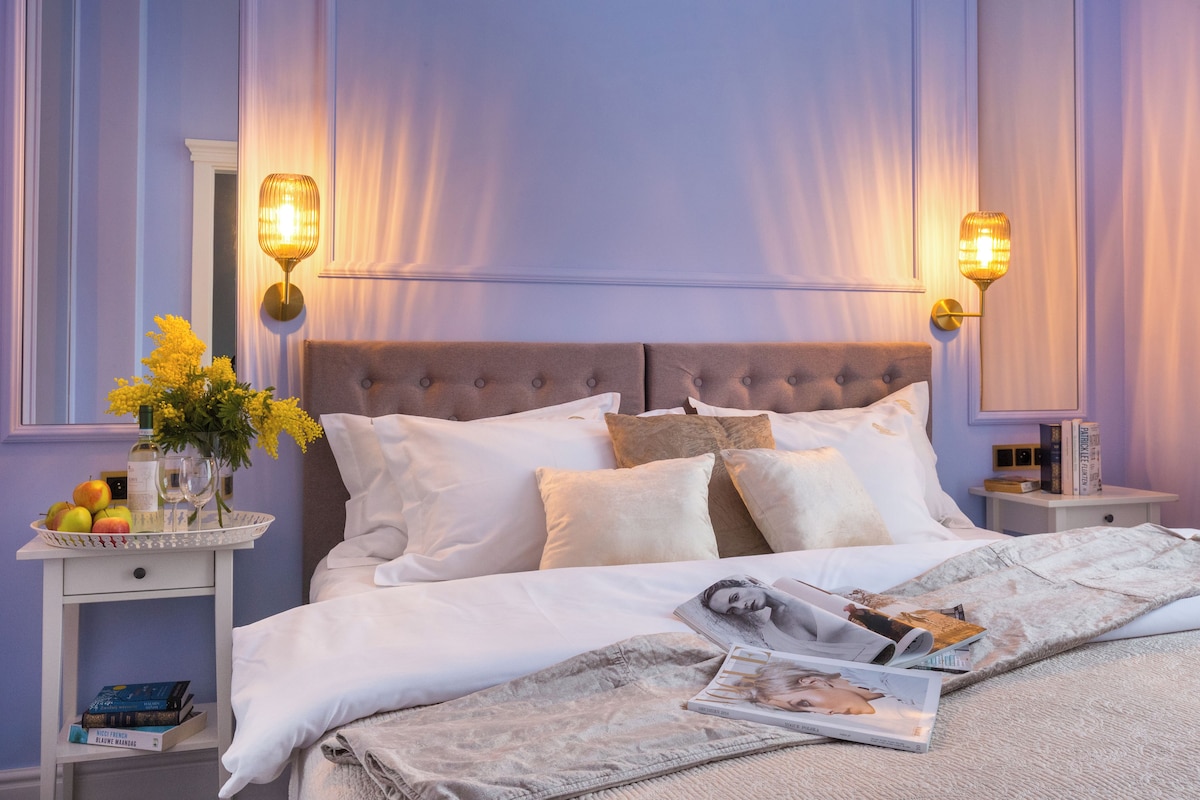 A neatly made bed with white linens, a bedside table with a lamp, and a magazine on the bed.
