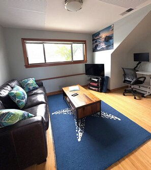 A living room with a leather couch, a wooden coffee table, a TV, and a desk with a computer. - Sweet and Private Apartment Close to Everything Beautiful and Fun! (El Granada)