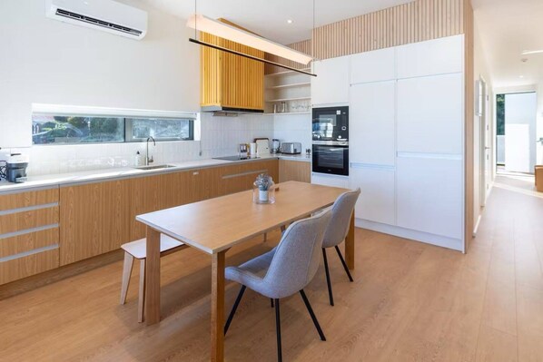 Una cocina moderna con armarios de madera, horno empotrado y comedor con mesa y sillas.