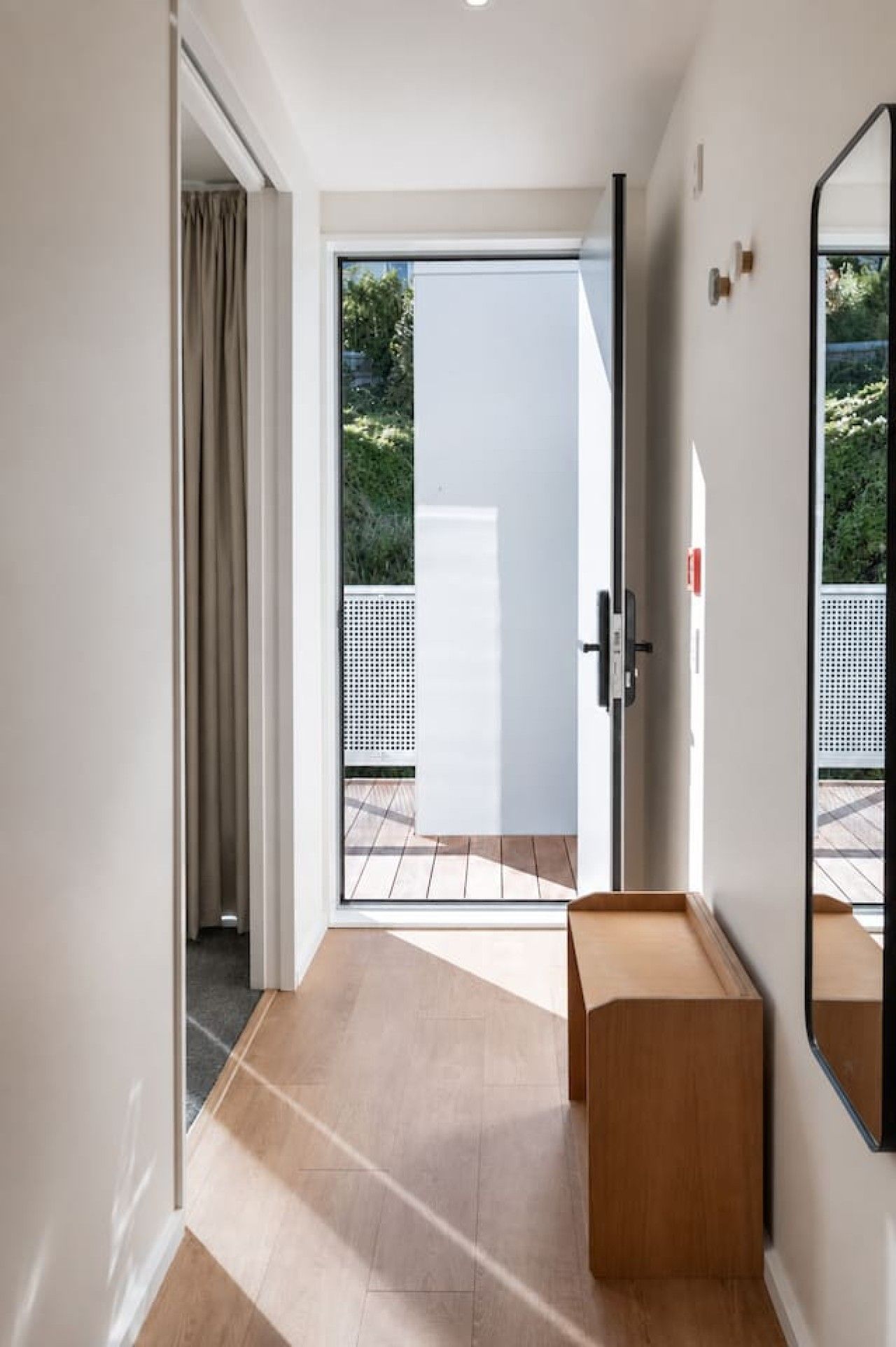 A modern interior with a sliding glass door leading to an outdoor area, a wooden bench, and a wall-mounted mirror.