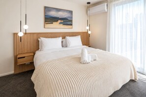 Ein Hotelzimmer mit einem Bett, einem Holzkopfteil, einem Gemälde an der Wand und einem Fenster mit Vorhängen.