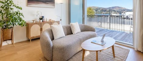 Una sala de estar moderna con un sofá, una mesa de centro, una planta en maceta, un armario y un ventanal con vistas al exterior.