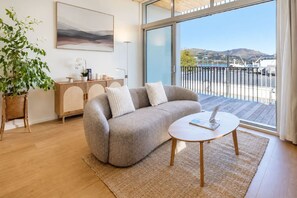 Una sala de estar moderna con un sofá, una mesa de centro, una planta en maceta, un armario y un ventanal con vistas al exterior.
