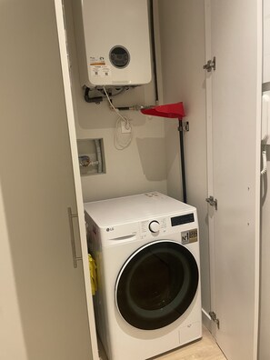 A compact laundry room with a white washing machine, a red drying rack, and a white wall-mounted heater. - Open-Concept 2-Bedroom Apartment in Puerta de Toledo, Berlany, Spain (Madrid)