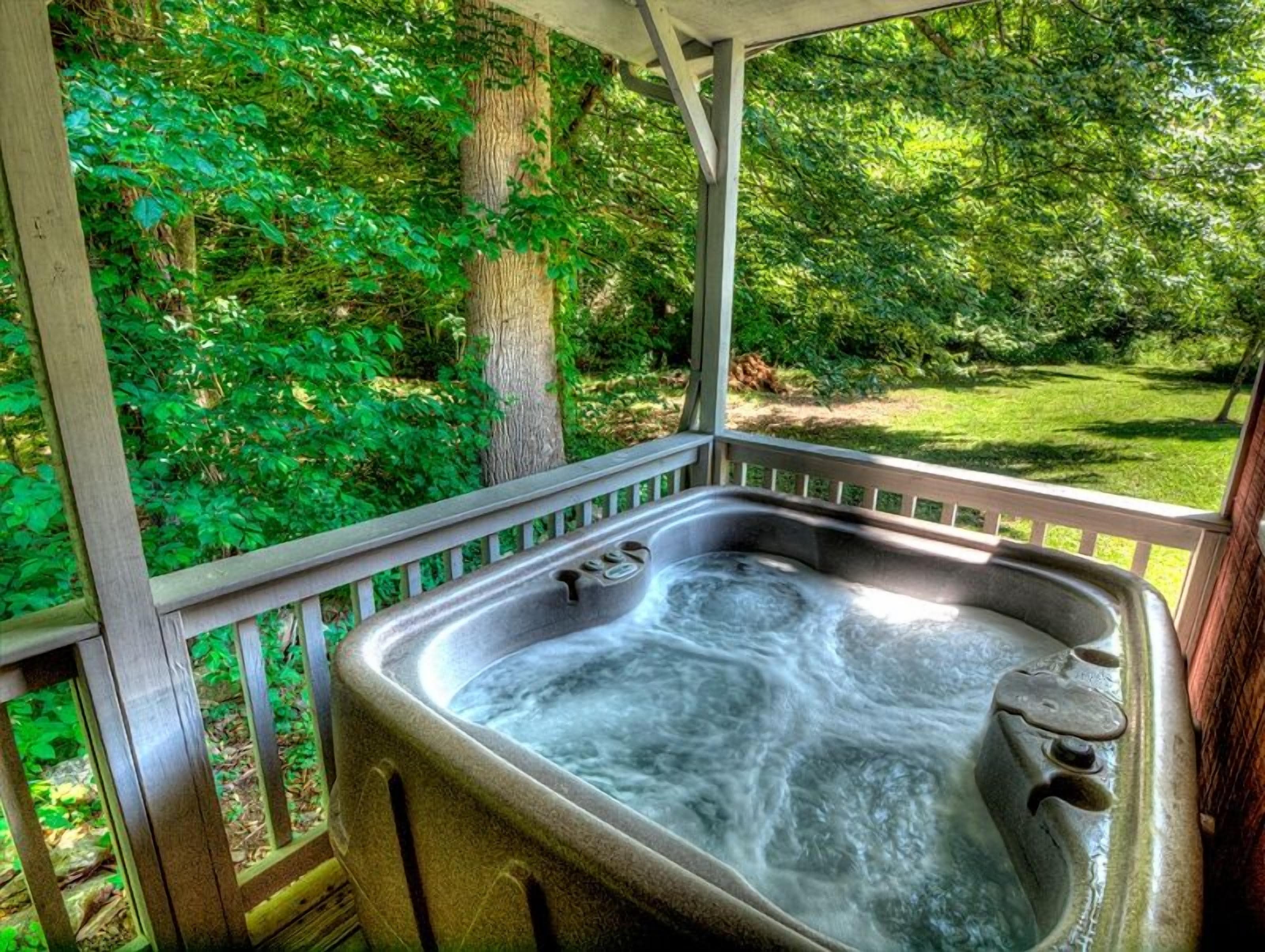 A hot tub on a wooden deck with a view of a lush green garden.