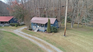 A blue house with a red roof, surrounded by a grassy yard and trees. - Bear Kottage Creekside Cabin (Bryson City)