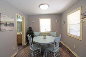 A dining room with a round table, four chairs, a small potted plant, a Christmas tree, and a window with blinds. - Captain's Bend Creekside Cabin (Bryson City)