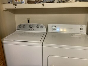 Two stacked white appliances, a washer and a dryer, with a shelf above containing folded clothes and a bottle. - Captain's Bend Creekside Cabin (Bryson City)