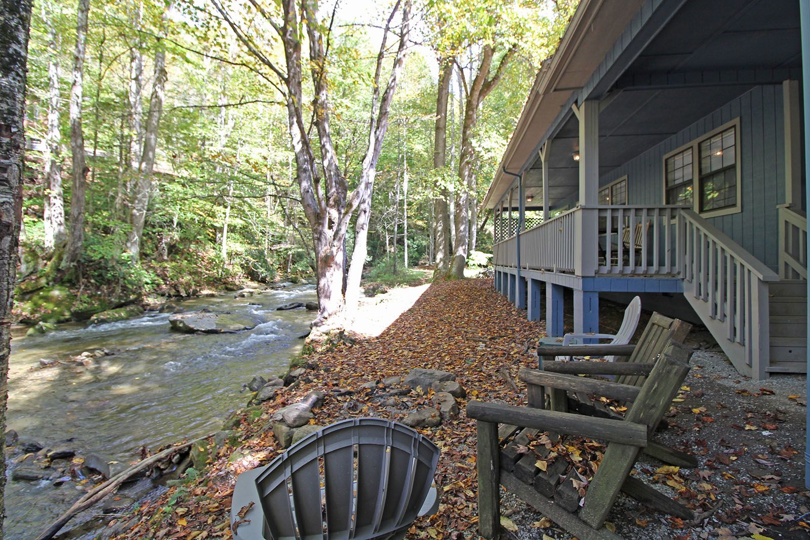 A cabin with a porch overlooking a forested area and a stream.