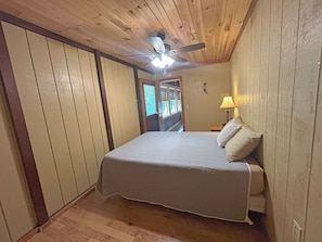 Quarto com cama, ventilador de teto e mesa de cabeceira com abajur.