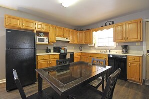 A kitchen with wooden cabinets, a black refrigerator, a microwave, a stove, and a dining table with chairs. - Wolf's Den Creekside Cabin (Bryson City)