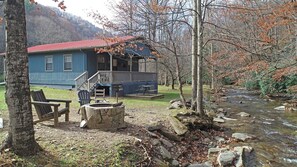 A cabin with a porch, a fire pit, and a stream. - Wolf's Den Creekside Cabin (Bryson City)