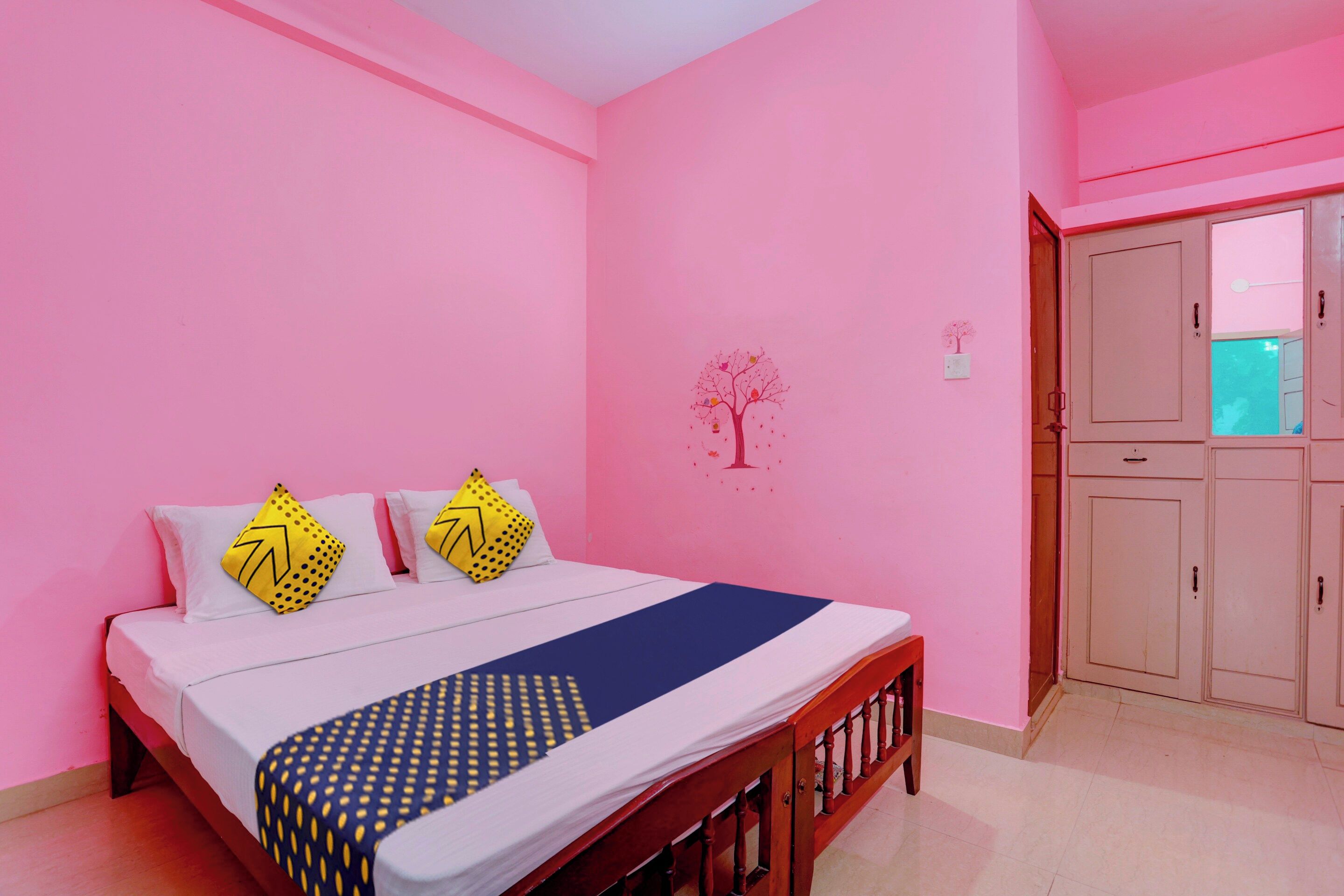 Un dormitorio con cama, almohadas, un adorno de árbol en la pared y un armario.
