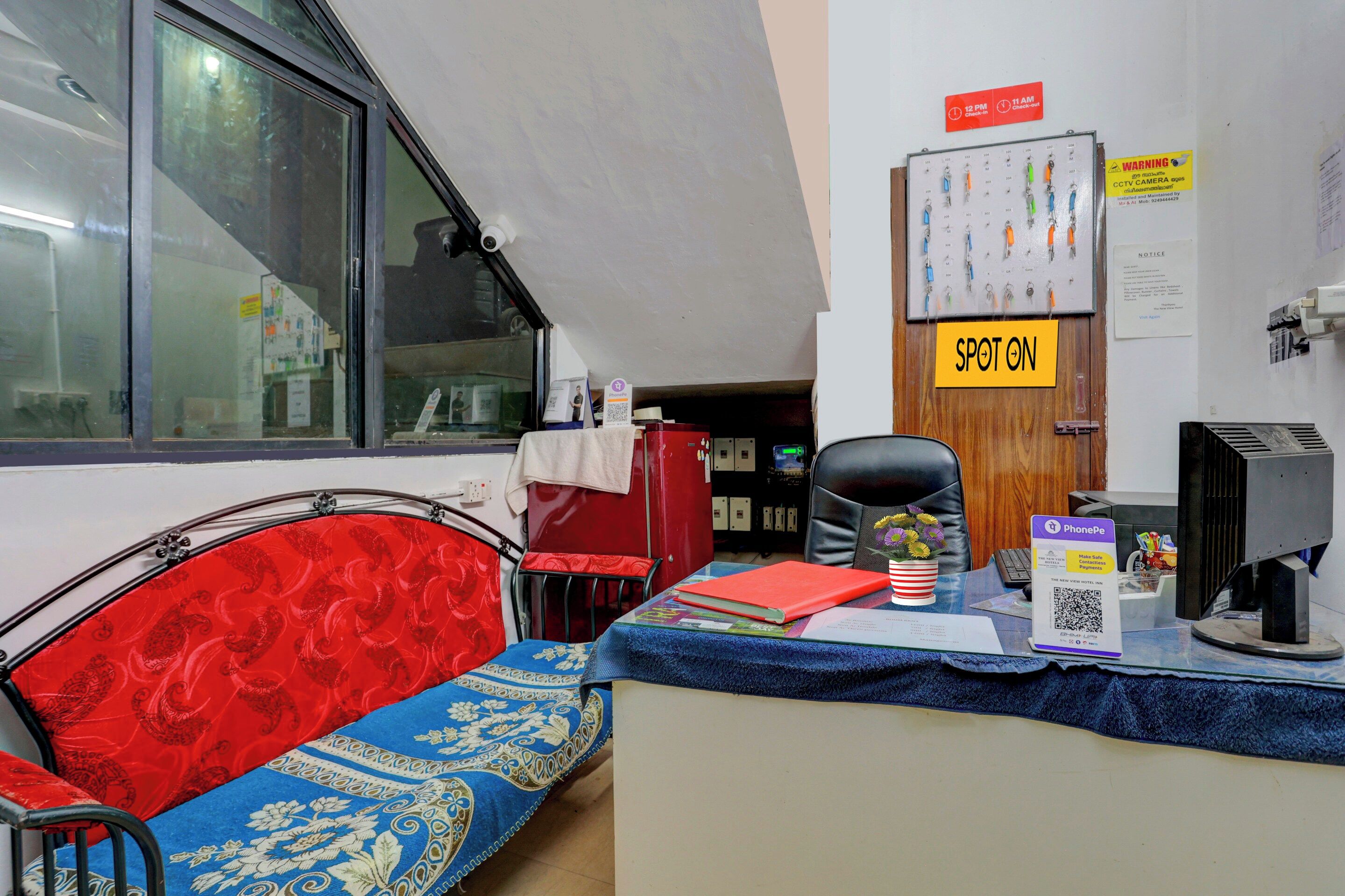 A hotel reception area with a desk, a chair, a sofa, a window, and a door.