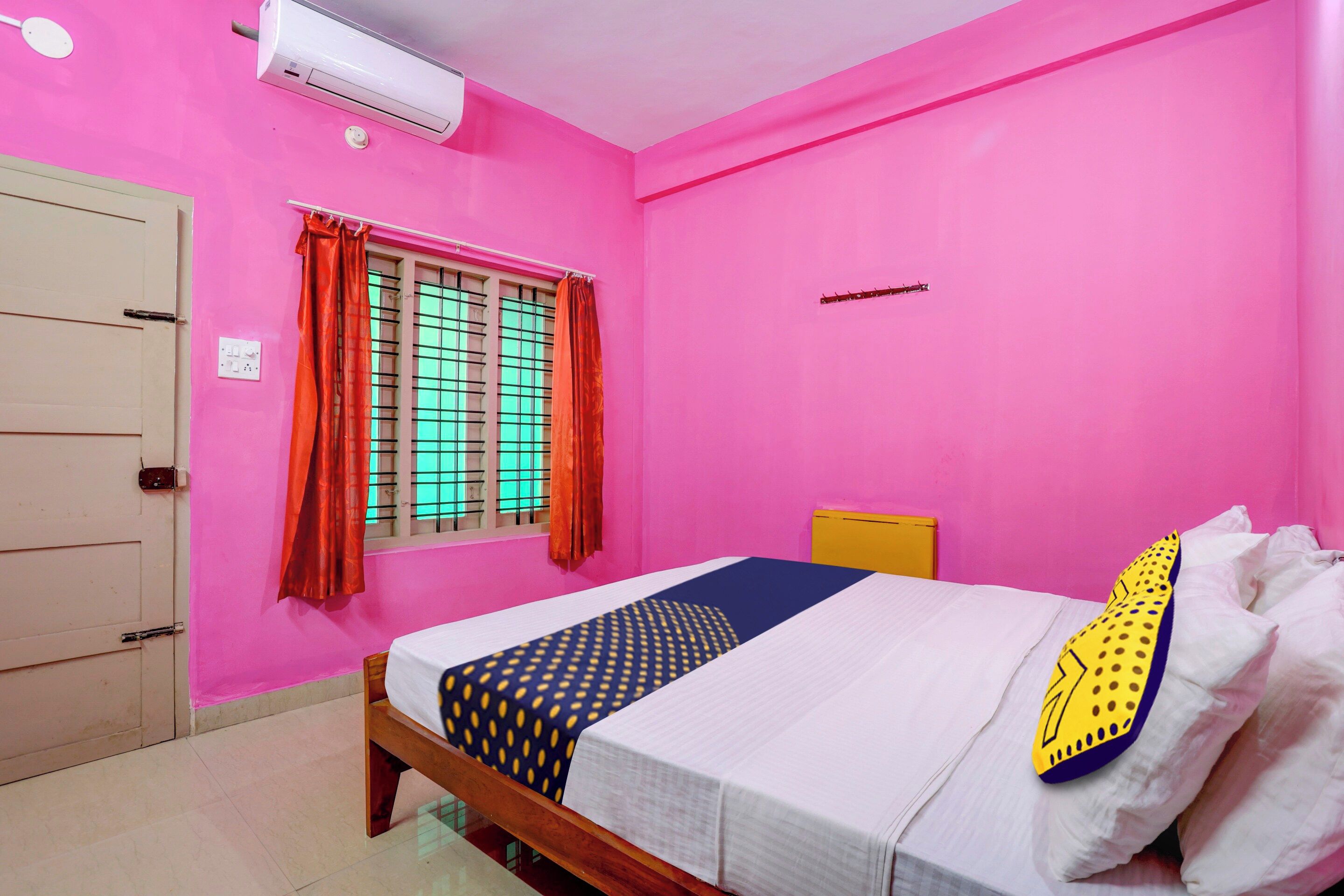 A room with a bed, a window with curtains, a wall-mounted air conditioner, and a door.