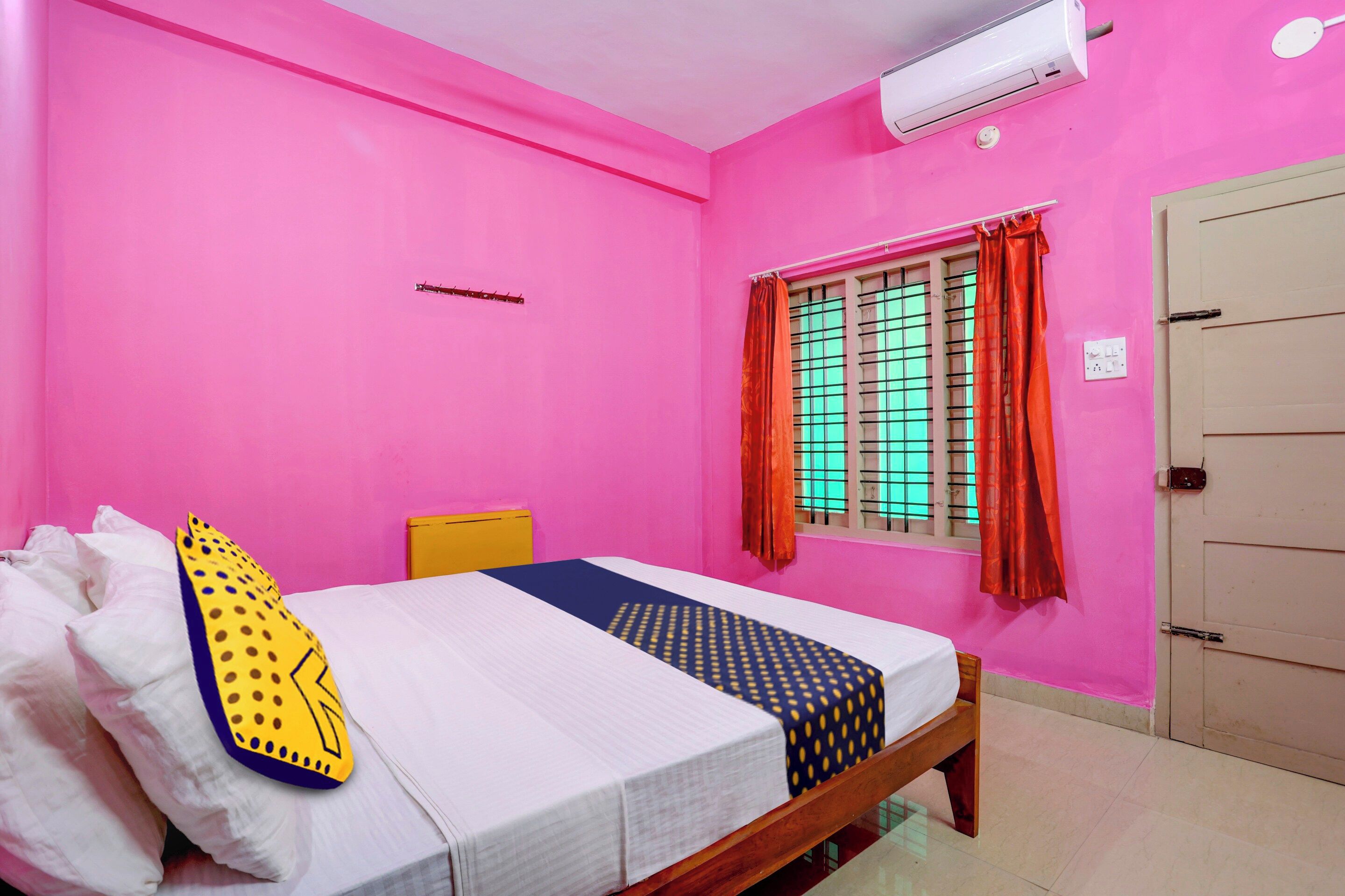 A room with a bed, a window with curtains, a wall-mounted air conditioner, and a door.