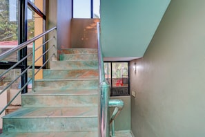 A staircase with metal railings and a handrail, leading to a landing with a red chair. - THE NEW VIEW HOTEL INN (Thiruvananthapuram)