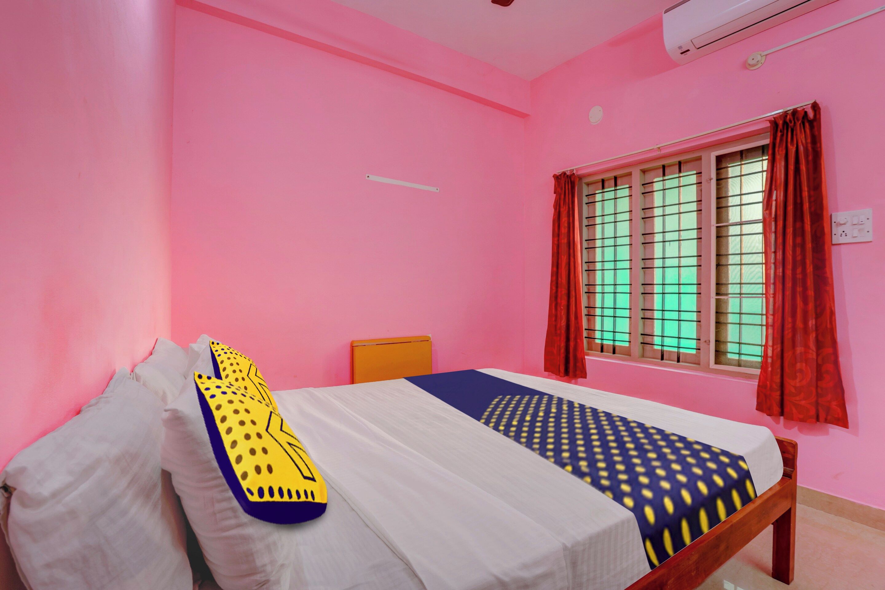 A room with pink walls, a bed with white and patterned bedding, a window with red curtains, and a ceiling fan.
