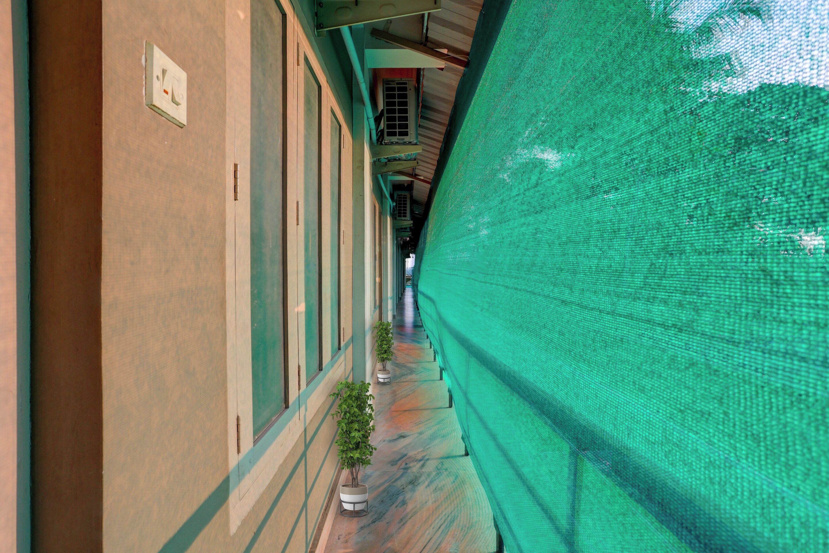 A corridor with a green netting on one side, a potted plant, and a door with a light switch.