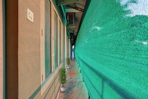 A corridor with a green netting on one side, a potted plant, and a door with a light switch. - THE NEW VIEW HOTEL INN (Thiruvananthapuram)