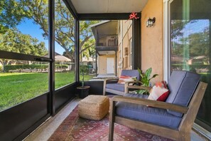 A sunlit room with a large window, a sofa, a small table, and a potted plant. - The Quiet Oak - Peaceful South Tampa Condo w/ Pool and Reflection Pond (Tampa)