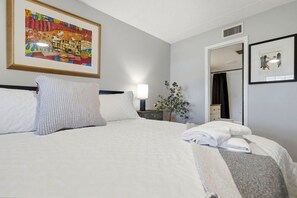 A hotel room with a large bed, a nightstand with a lamp, a framed picture on the wall, and a door leading to a bathroom. - The Quiet Oak - Peaceful South Tampa Condo w/ Pool and Reflection Pond (Tampa)