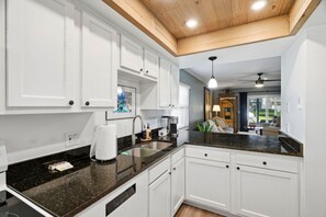 A modern kitchen with white cabinets, a granite countertop, and a built-in dishwasher. - The Quiet Oak - Peaceful South Tampa Condo w/ Pool and Reflection Pond (Tampa)