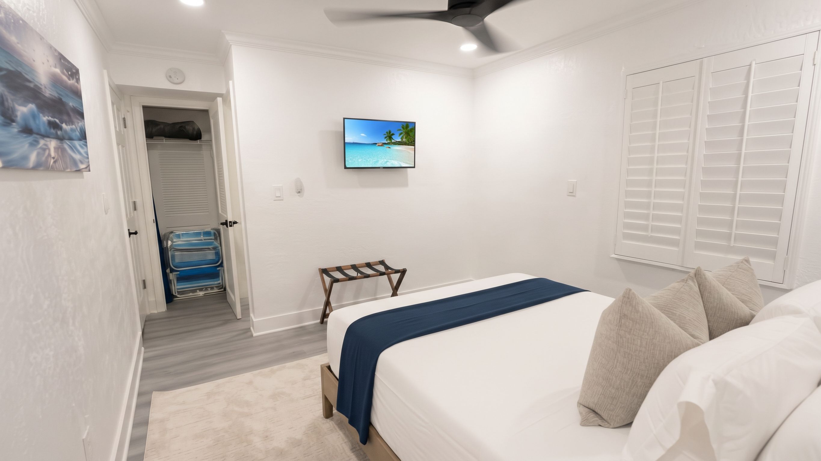 Une chambre à coucher avec un lit, un téléviseur fixé au mur, une porte donnant sur un placard et une fenêtre avec des stores.