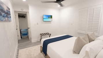 Une chambre à coucher avec un lit, un téléviseur fixé au mur, une porte donnant sur un placard et une fenêtre avec des stores.